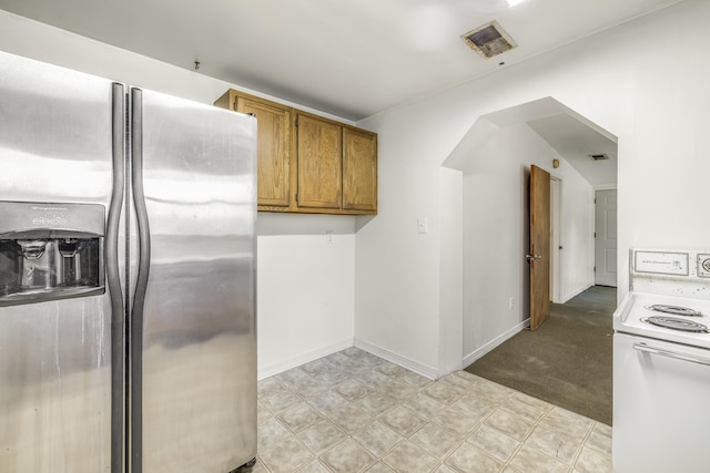 kitchen featuring light carpet, stainless steel fridge, white electric stove, baseboards, and brown cabinetry