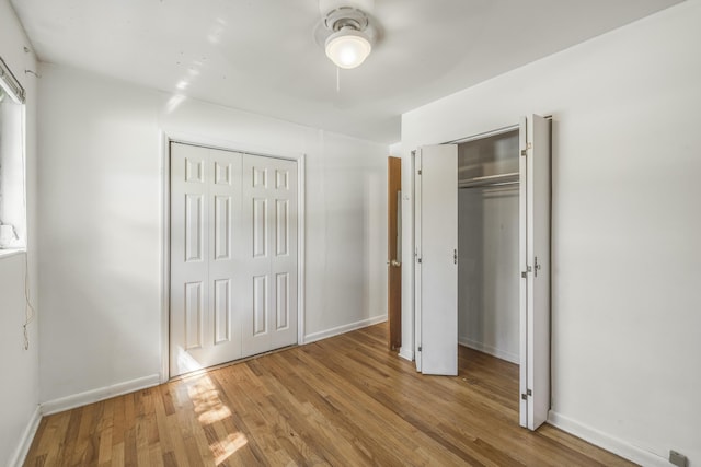 unfurnished bedroom with wood finished floors, ceiling fan, baseboards, and two closets