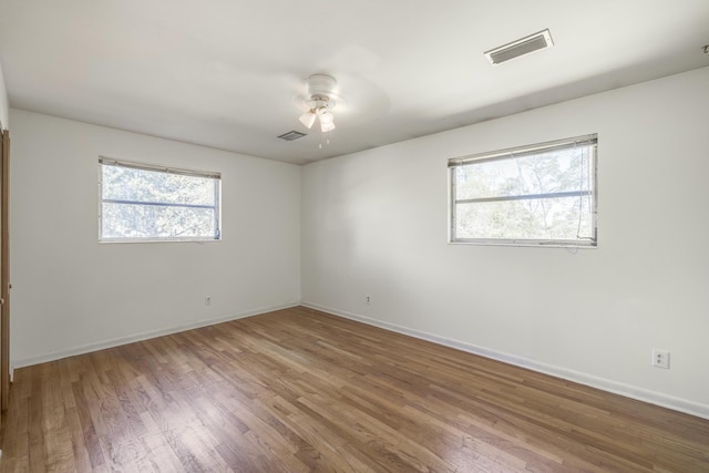 empty room with ceiling fan, wood finished floors, visible vents, and baseboards