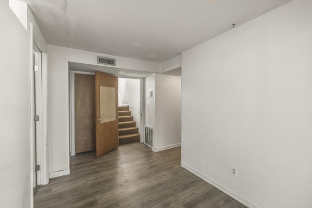 spare room featuring wood finished floors, visible vents, baseboards, and stairs