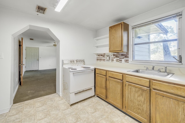 kitchen with white range with electric stovetop, arched walkways, open shelves, light countertops, and a sink