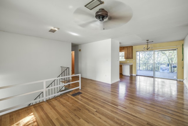 empty room featuring light wood-type flooring, visible vents, baseboards, and ceiling fan with notable chandelier