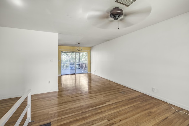 unfurnished room featuring ceiling fan with notable chandelier, wood finished floors, visible vents, and baseboards