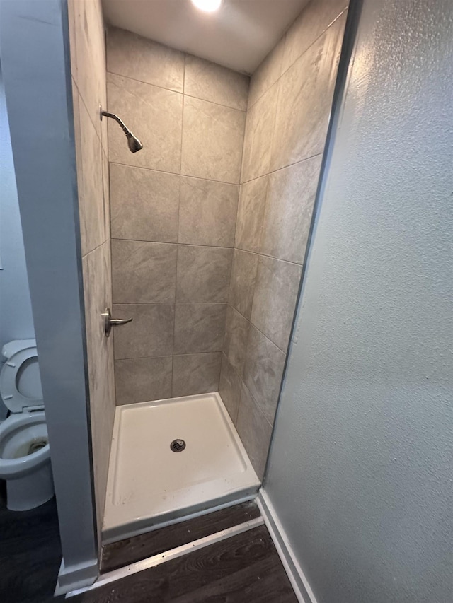 bathroom with wood-type flooring, toilet, and tiled shower