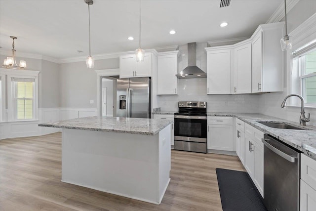 kitchen featuring white cabinets, wall chimney range hood, decorative light fixtures, and appliances with stainless steel finishes