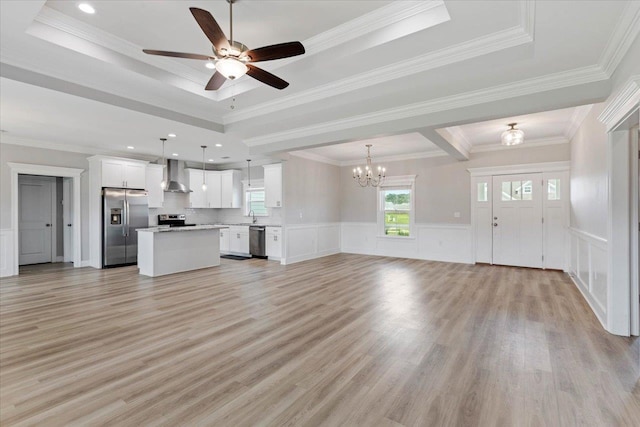 unfurnished living room with ornamental molding, light wood-type flooring, ceiling fan with notable chandelier, and a tray ceiling