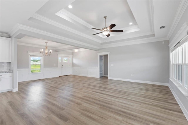 unfurnished living room featuring light wood-type flooring, ceiling fan with notable chandelier, a raised ceiling, and crown molding