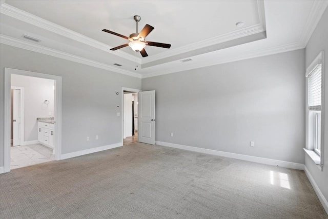 unfurnished bedroom with ornamental molding, ensuite bathroom, ceiling fan, and a tray ceiling