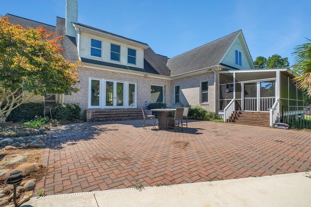 back of property with a sunroom, a patio area, brick siding, and a chimney