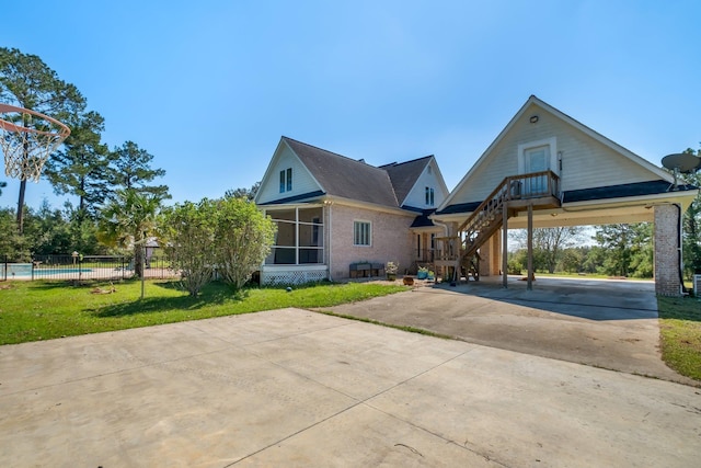 view of front facade with brick siding, a sunroom, fence, driveway, and a front lawn