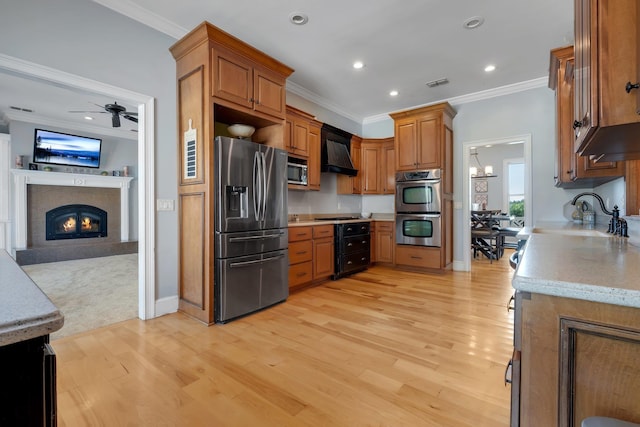 kitchen with stainless steel appliances, a sink, open floor plan, light countertops, and wall chimney exhaust hood