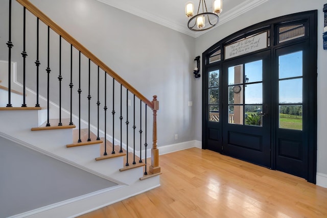 entrance foyer with an inviting chandelier, ornamental molding, wood finished floors, baseboards, and stairs