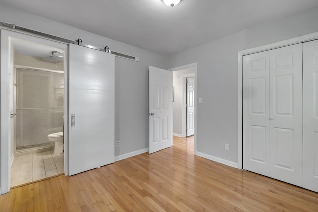 unfurnished bedroom with ensuite bathroom, a barn door, light wood-type flooring, and a closet