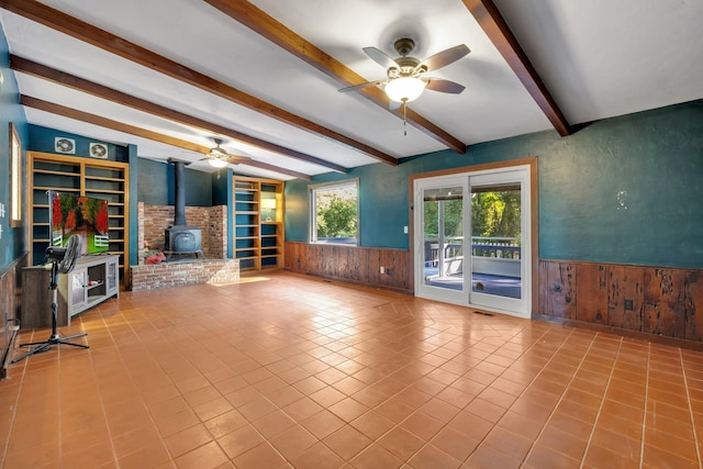 unfurnished living room featuring light tile patterned floors, vaulted ceiling with beams, a wood stove, and ceiling fan