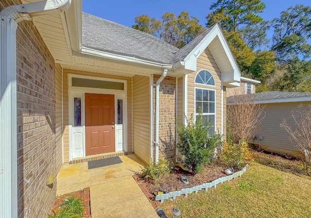 doorway to property featuring a shingled roof and brick siding