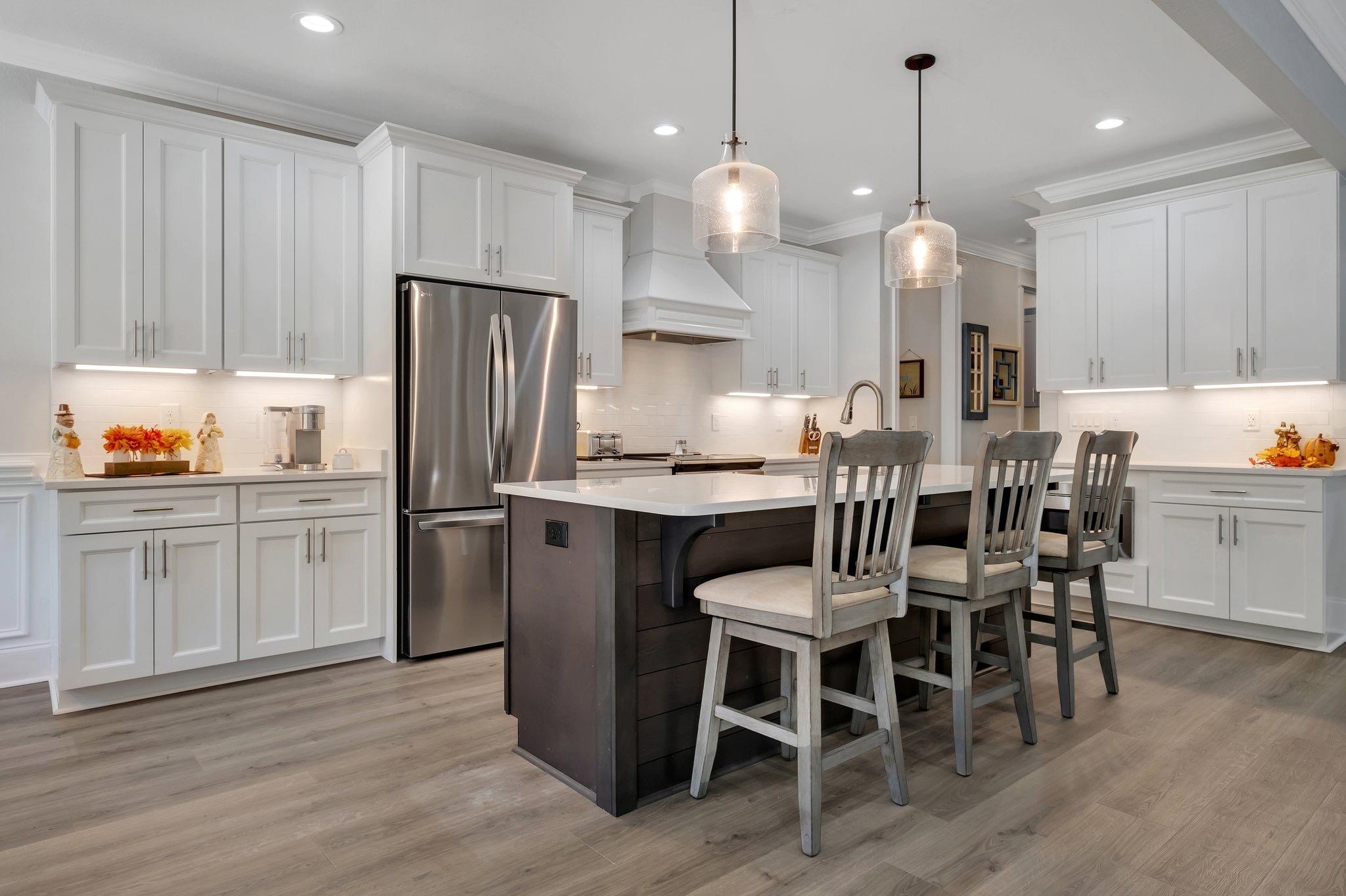 kitchen with a center island with sink, custom range hood, decorative light fixtures, white cabinetry, and stainless steel refrigerator