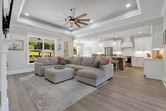 living room featuring a tray ceiling, light hardwood / wood-style flooring, ceiling fan, and ornamental molding