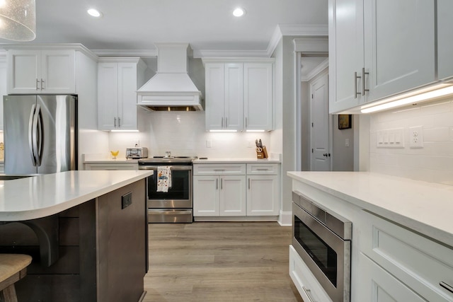 kitchen with white cabinets, appliances with stainless steel finishes, light hardwood / wood-style flooring, and custom exhaust hood