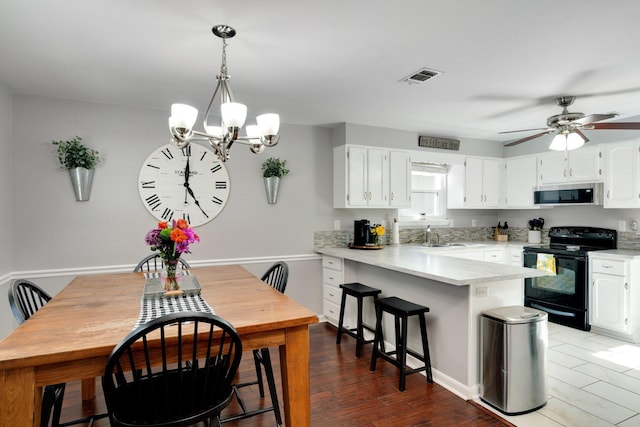 kitchen with kitchen peninsula, pendant lighting, black range with electric stovetop, ceiling fan with notable chandelier, and white cabinets