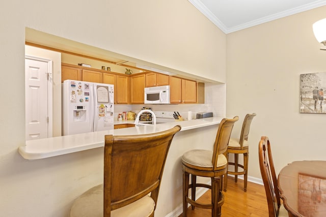 kitchen with a kitchen bar, ornamental molding, kitchen peninsula, white appliances, and light hardwood / wood-style flooring