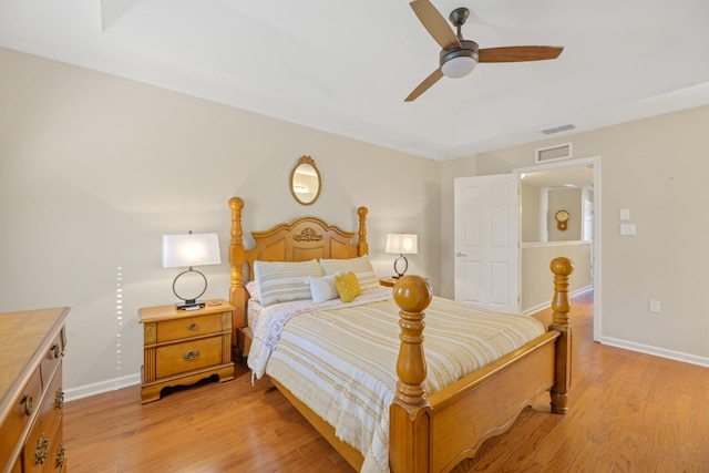 bedroom with light wood-type flooring, ceiling fan, and a tray ceiling