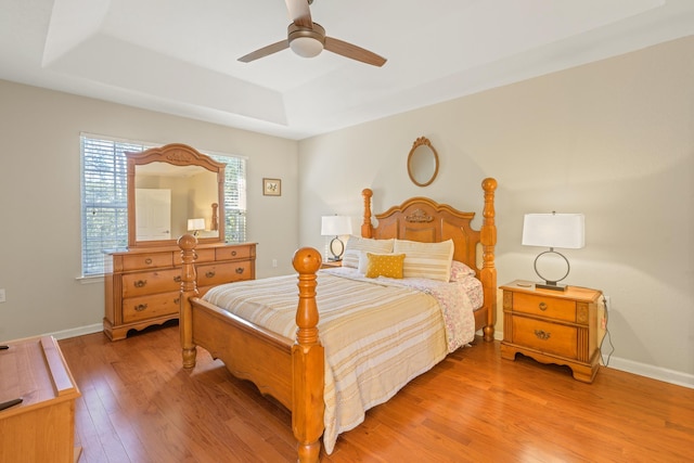 bedroom with ceiling fan, a tray ceiling, and light wood-type flooring