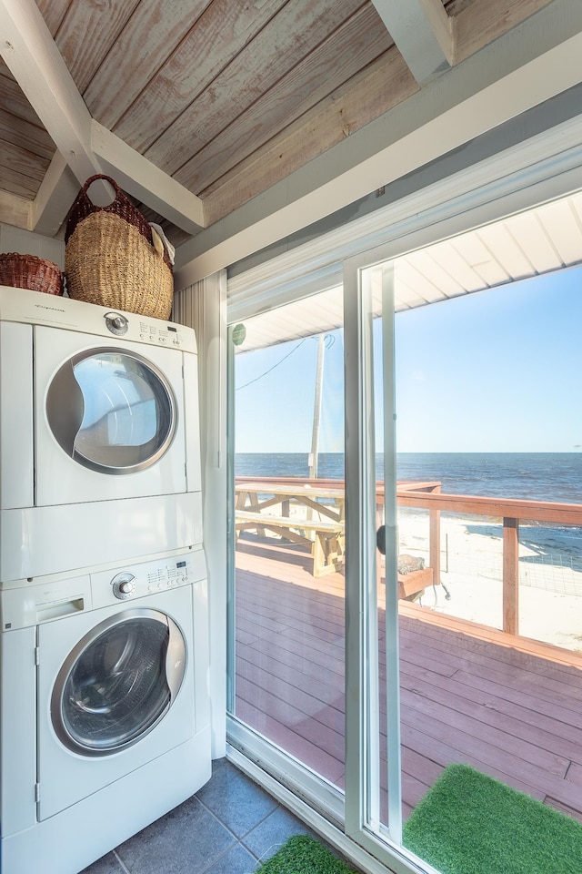 laundry area with a view of the beach, a water view, stacked washer and clothes dryer, and wooden ceiling