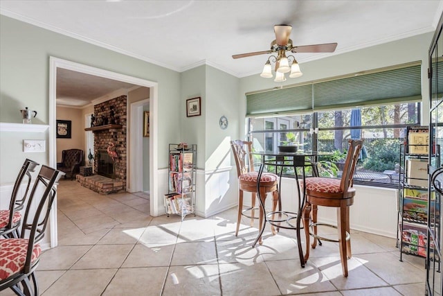 dining space with light tile patterned floors, a fireplace, ornamental molding, and a ceiling fan