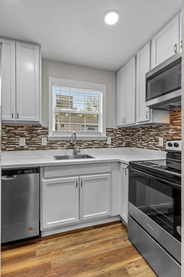 kitchen featuring sink, light wood-type flooring, stainless steel appliances, decorative backsplash, and white cabinets