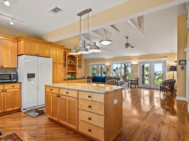 kitchen featuring lofted ceiling with beams, light stone counters, white fridge with ice dispenser, and french doors