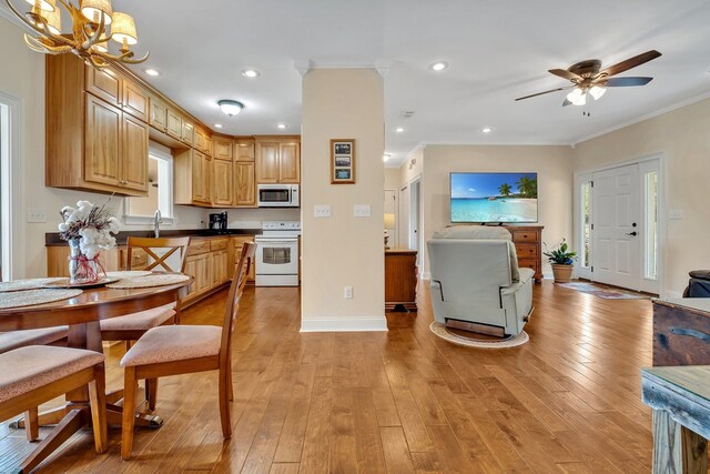 kitchen with ornamental molding, light hardwood / wood-style flooring, pendant lighting, white appliances, and ceiling fan with notable chandelier