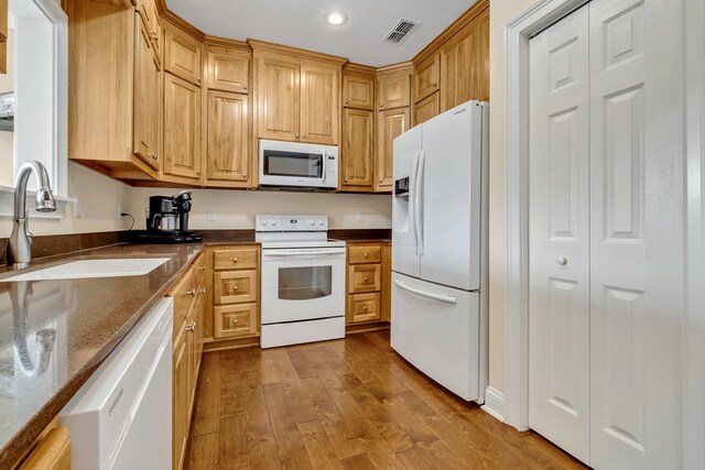 kitchen featuring dark stone counters, hardwood / wood-style flooring, white appliances, and sink