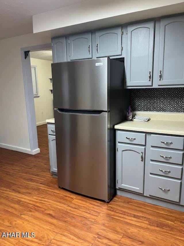 kitchen featuring light wood-style flooring, baseboards, light countertops, backsplash, and freestanding refrigerator