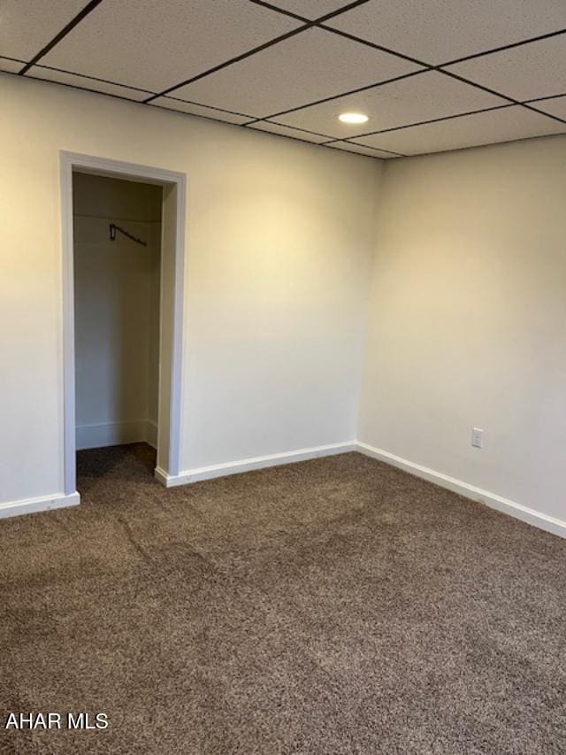 spare room featuring dark colored carpet, a drop ceiling, and baseboards