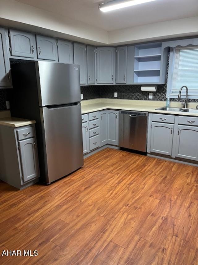 kitchen with stainless steel appliances, a sink, gray cabinetry, and wood finished floors