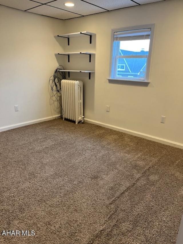 carpeted empty room with radiator heating unit, baseboards, and a drop ceiling