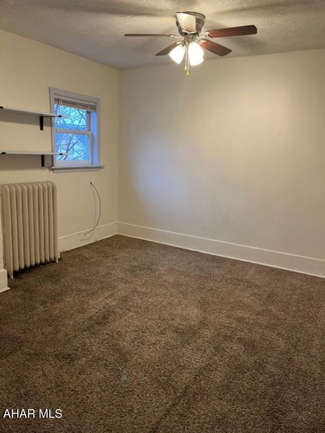 unfurnished room with a textured ceiling, dark carpet, baseboards, and radiator