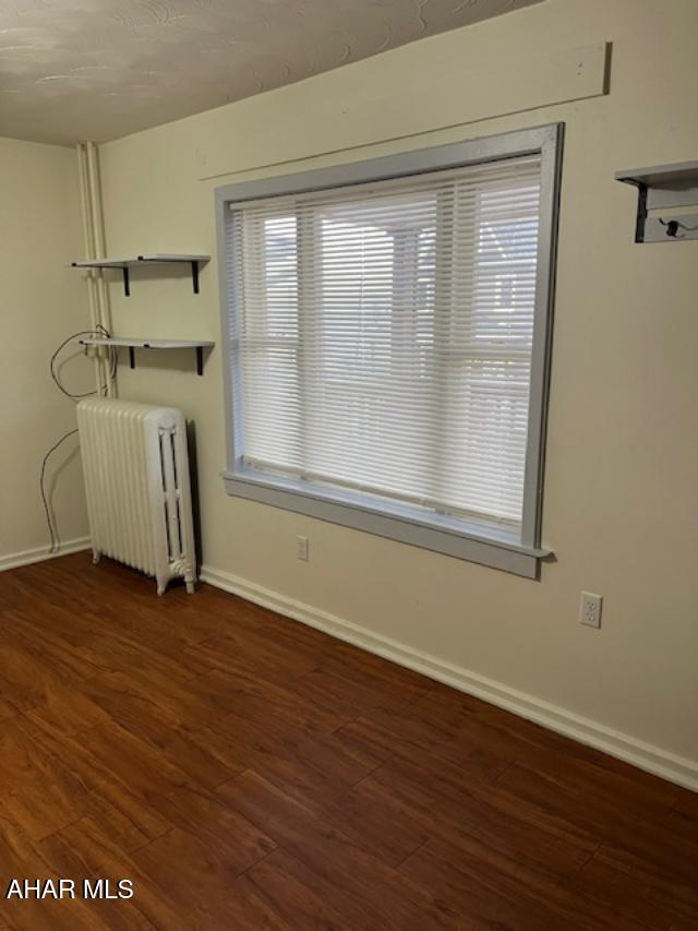 unfurnished room featuring baseboards, wood finished floors, and radiator