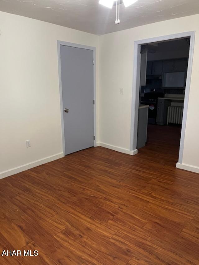 unfurnished room featuring dark wood-type flooring and baseboards