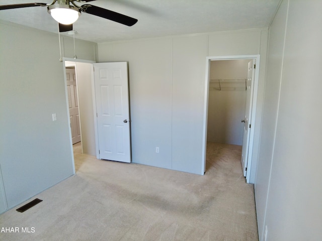 unfurnished bedroom with a walk in closet, ceiling fan, a closet, and light carpet