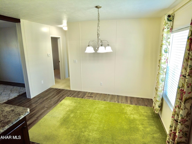 unfurnished dining area featuring dark wood-type flooring, a healthy amount of sunlight, and a notable chandelier