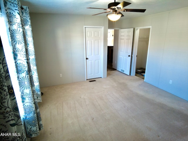 unfurnished bedroom featuring a walk in closet, ceiling fan, and light carpet