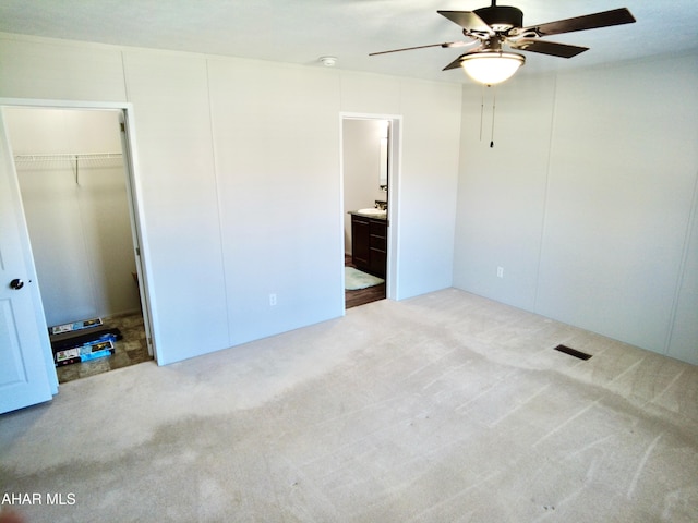 unfurnished bedroom with ensuite bath, ceiling fan, a closet, and light carpet