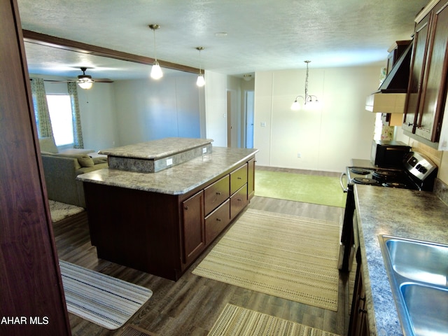 kitchen featuring a textured ceiling, dark wood-type flooring, sink, a kitchen island, and hanging light fixtures