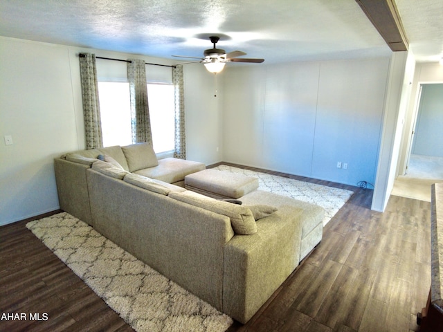 living room with a textured ceiling, ceiling fan, and dark wood-type flooring