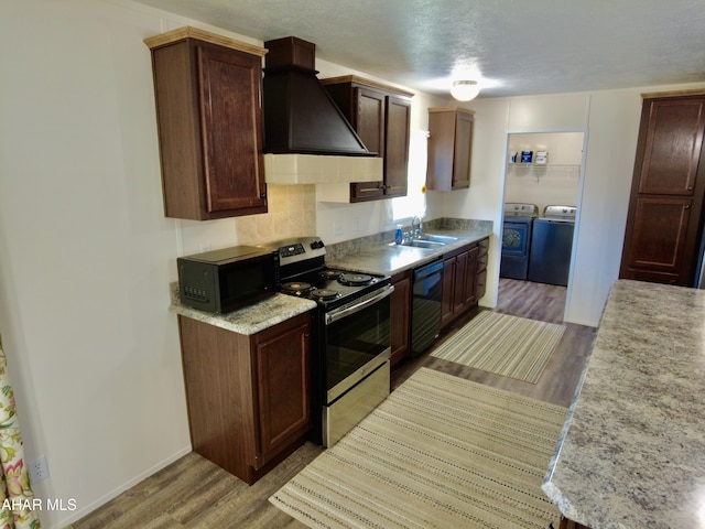 kitchen with light wood-type flooring, custom exhaust hood, sink, black appliances, and independent washer and dryer