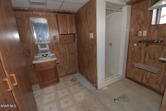 bathroom with vanity, tiled shower, and wood walls