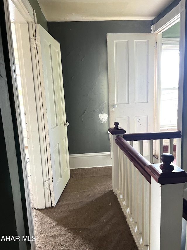 hall featuring baseboards and dark colored carpet