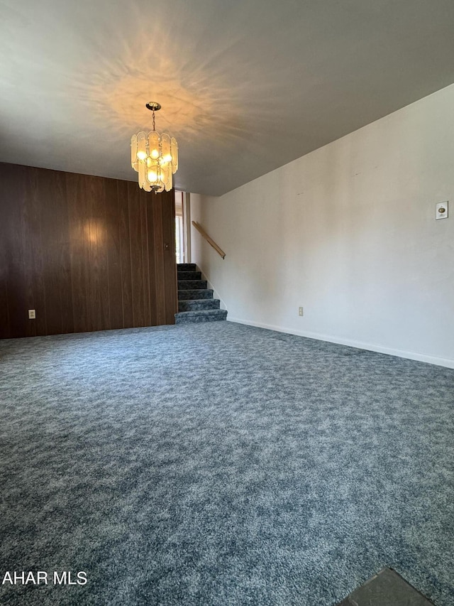 unfurnished living room featuring wooden walls, a chandelier, and dark colored carpet