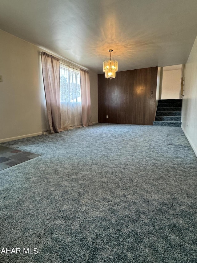 carpeted spare room with a chandelier and wooden walls